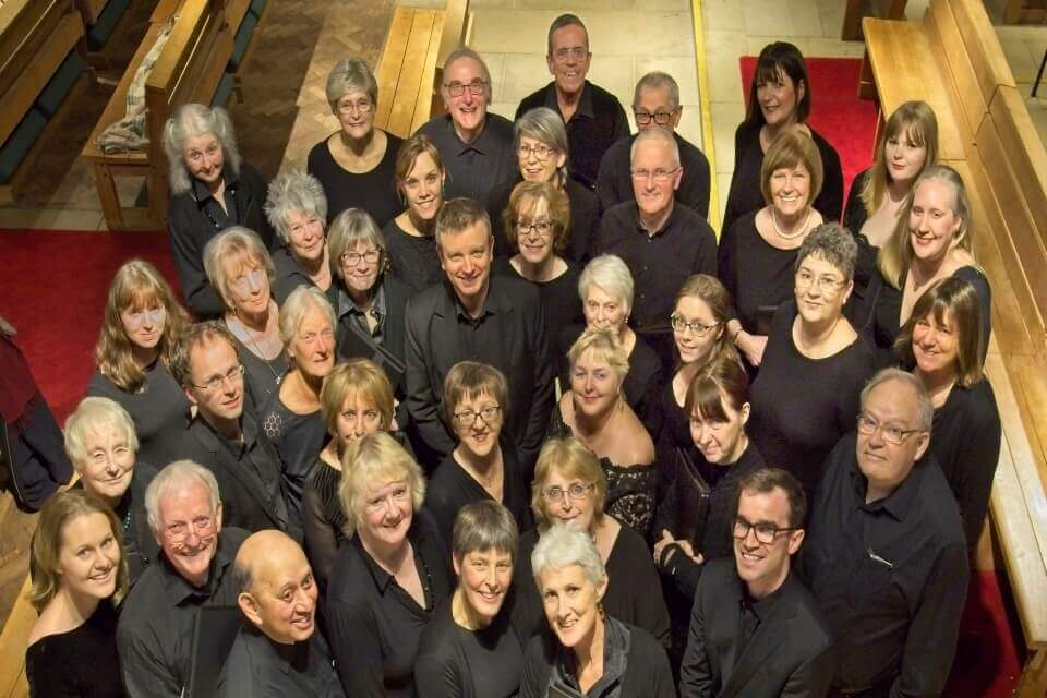 Photograph shows a collective of people (members of Keele Bach Choir) grouped together looking up